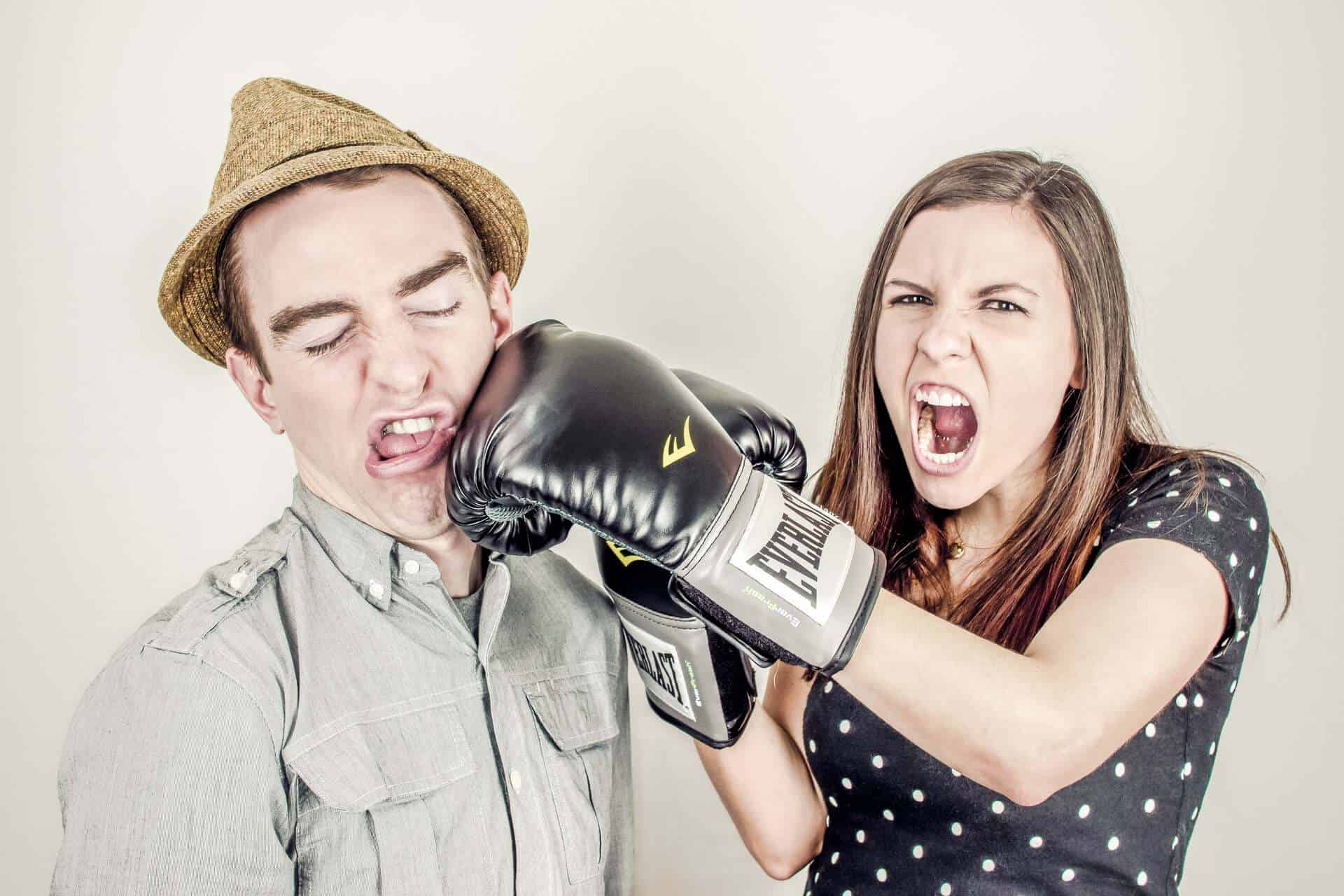 Girl punching guy while wearing boxing gloves, confrontation between the two.