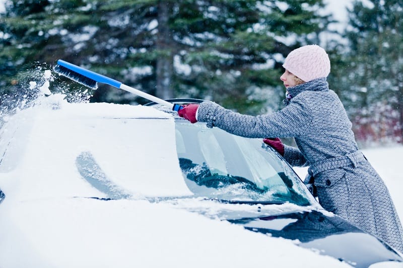 Woman Removing Snow from a Car with a Broom after the snow storm