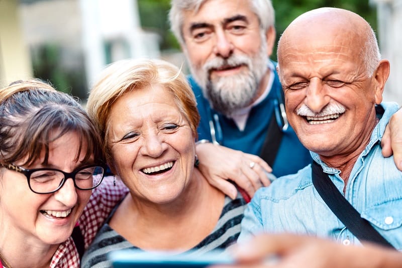 Happy senior friends taking selfie around old town street - Retired people having fun together with mobile phone - Positive elderly lifestyle concept with focus on blond woman