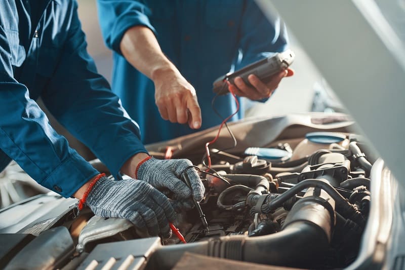 Close-up image of professional mechanics testing car battery with multimeter